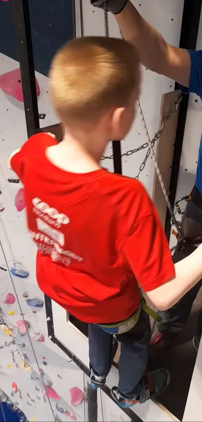 A young climber in a red shirt climbs an indoor wall with colorful holds.