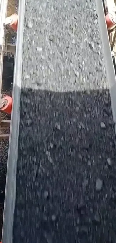 Conveyor belt with dark stones on industrial background.