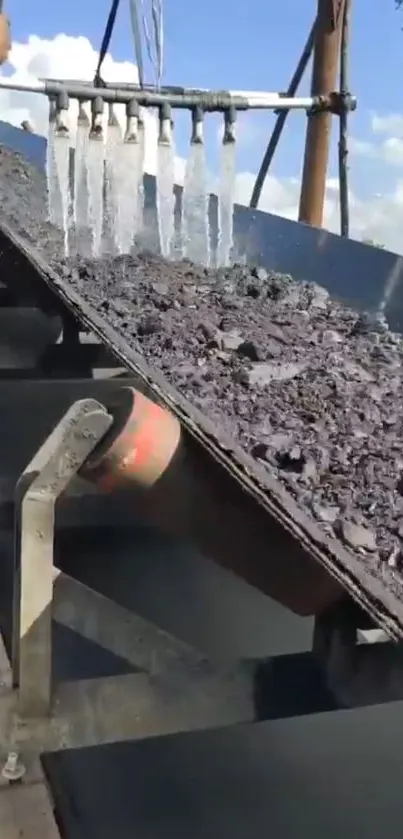 Conveyor belt with raw materials and water streams under blue sky.