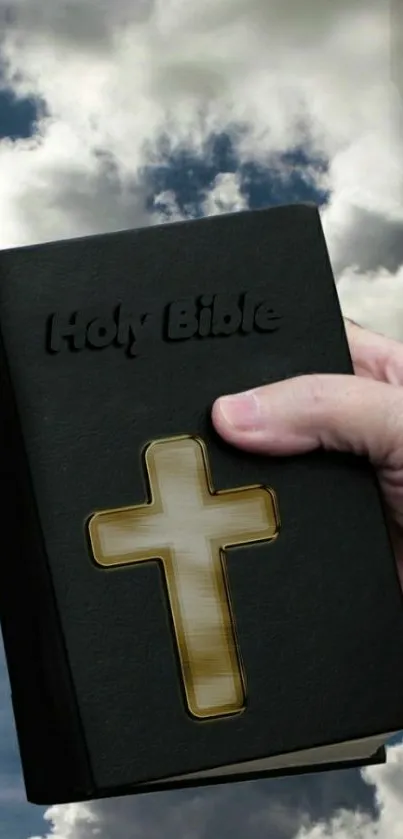 Hand holding Holy Bible with cross in cloudy sky wallpaper.