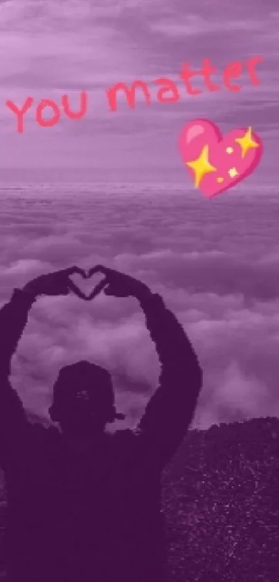 Silhouette forming heart with hands over a purple mountain landscape.