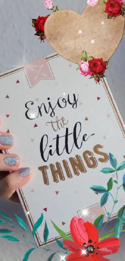Hand holding a card with 'Enjoy the little things' text and floral designs.