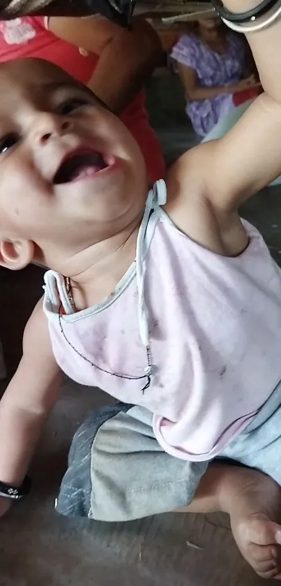 Smiling baby reaching upwards wearing a white outfit on the floor.