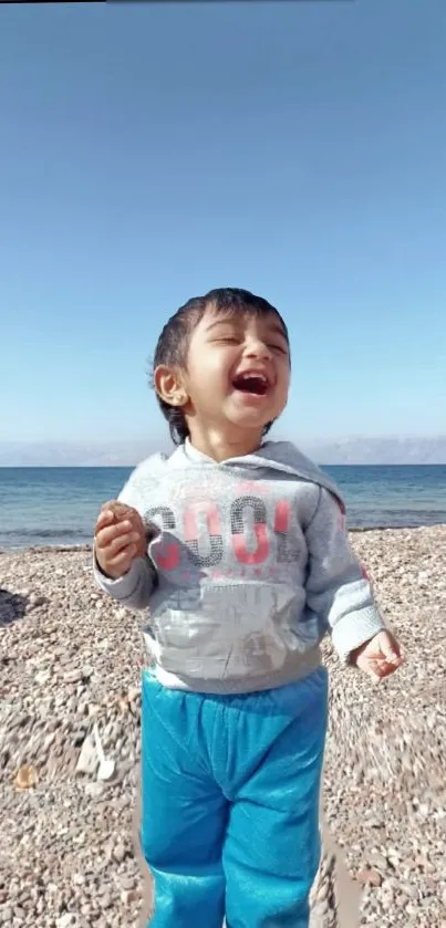 Child laughing on a sunny beach with blue sky and ocean backdrop.