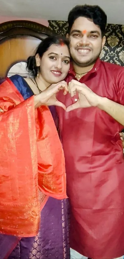 Smiling couple creating heart with hands in traditional attire.