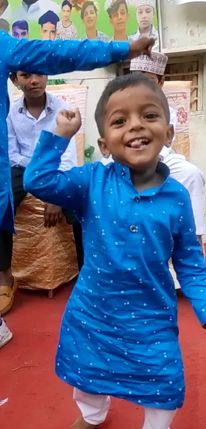 Joyful child in blue kurta dancing on red carpet.