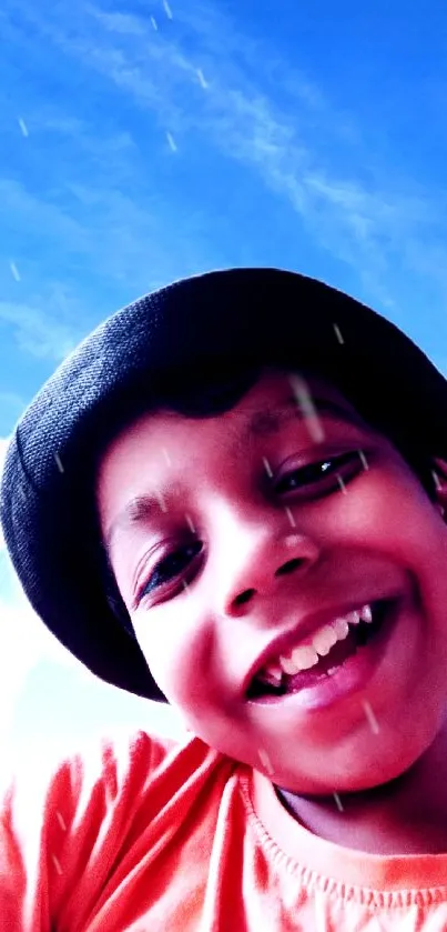 Smiling child under a clear blue sky wearing a black hat and orange shirt.