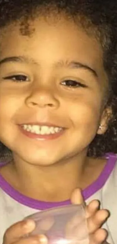 A smiling child with curly hair holding a cup.