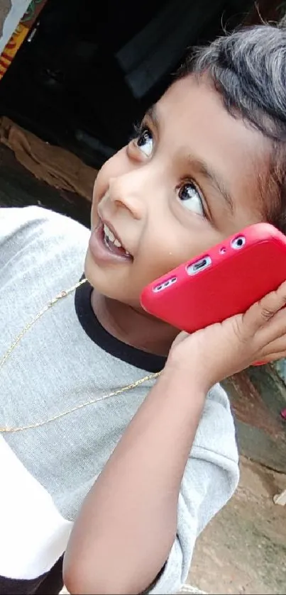 A joyful child with a red phone smiling outdoors.