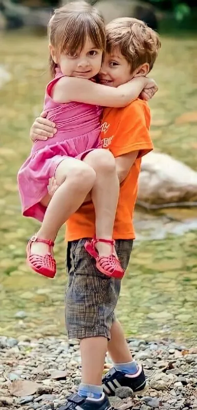 Two children joyfully embrace by a forest stream.