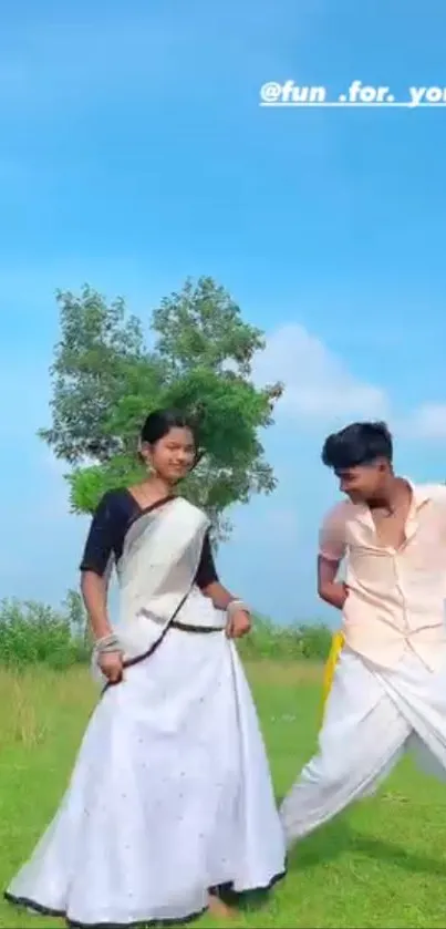 Two people dancing joyfully in a meadow with a blue sky backdrop.