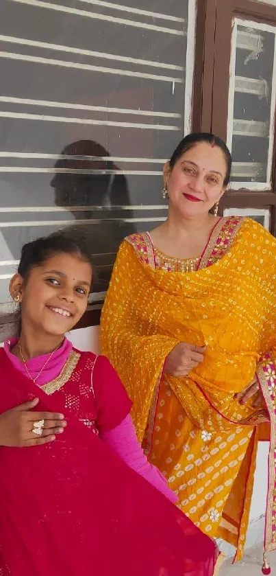 Mother and daughter in colorful traditional attire, smiling happily.