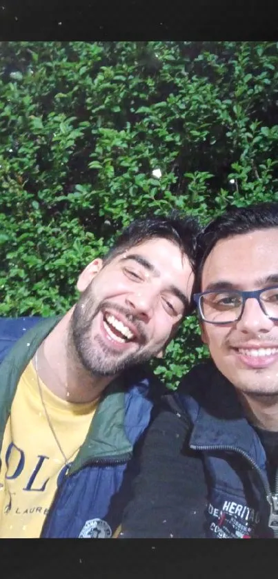 Two friends enjoying laughter in nature with a green backdrop.