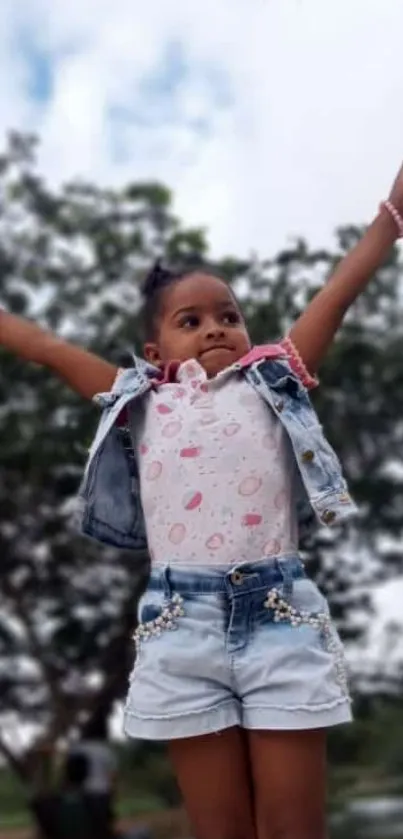 Young girl joyfully raising arms with green background.