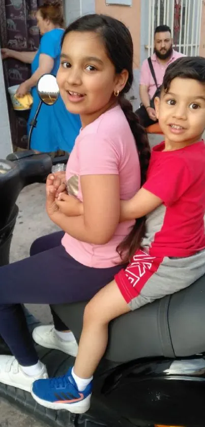 Children joyfully sitting on a scooter in a vibrant street scene.