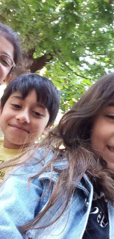 Smiling children under green leafy trees.