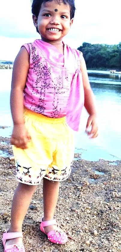 Smiling child in colorful dress standing by the seaside.