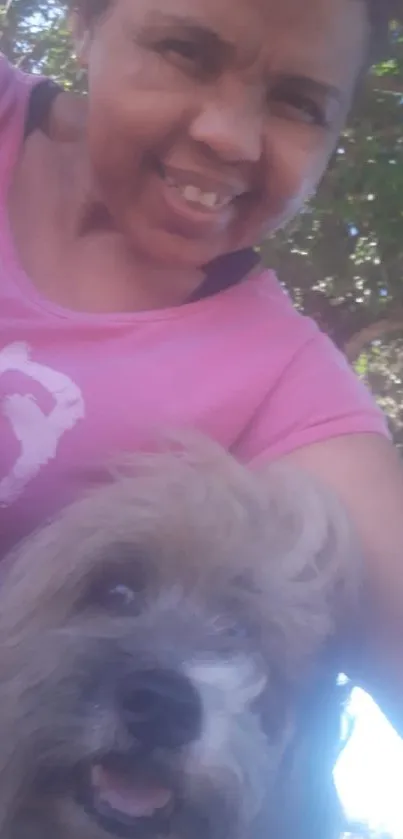 Smiling person with a dog outdoors in a pink shirt.