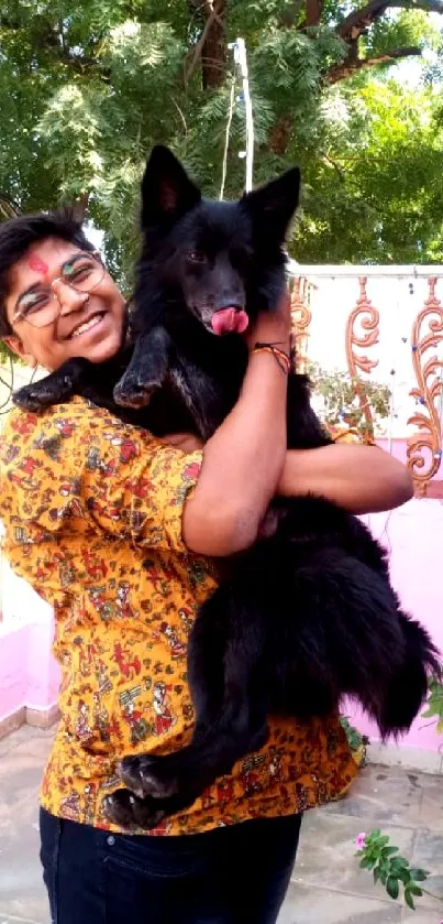 Person joyfully holding a black dog outdoors with vibrant greenery.