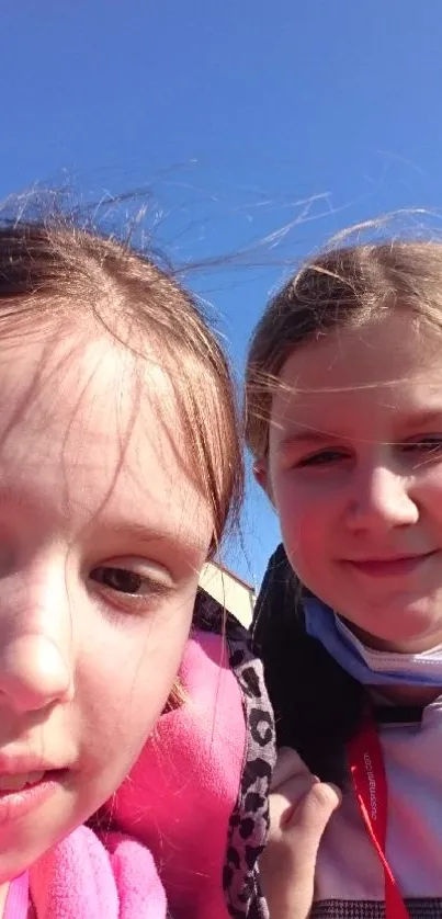 Two kids smiling under a clear blue sky, enjoying a sunny day outdoors.