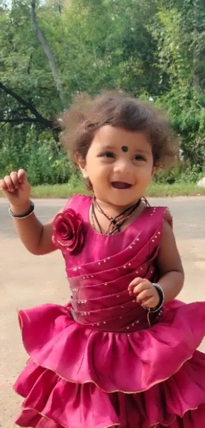 Joyful toddler in pink dress with green forest backdrop.