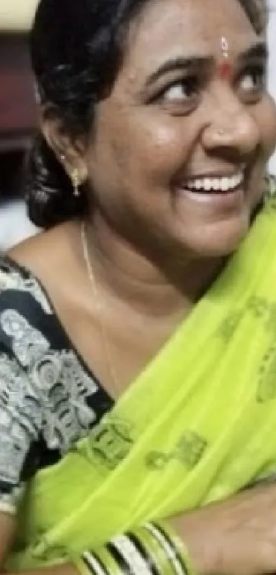 Smiling woman wearing a green saree with traditional patterns.