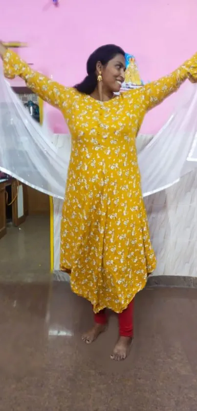 Woman in a yellow floral dress joyfully posing indoors.