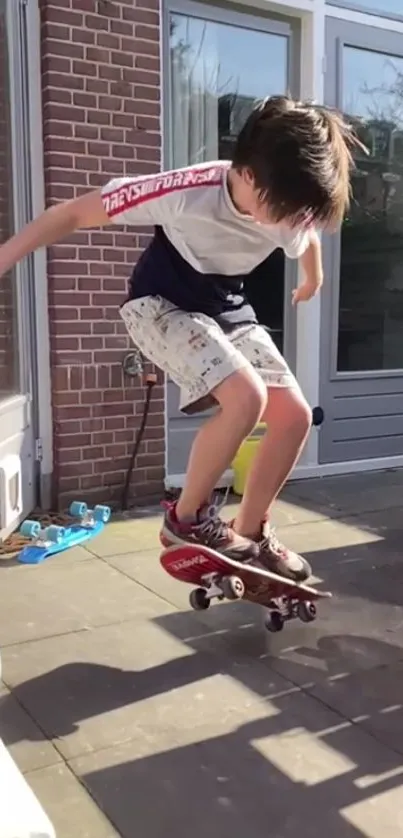 Child skateboarding on patio with brick wall backdrop.