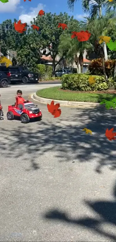 Kids ride toy cars under autumn leaves in sunny park.