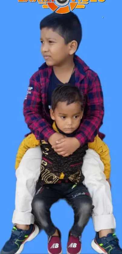 Two kids sitting on each other against a bright blue background.