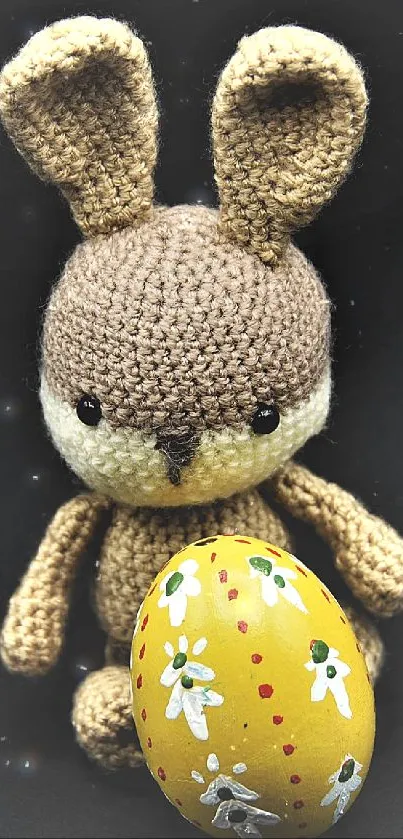 Knitted bunny holding a festive Easter egg on a black background.