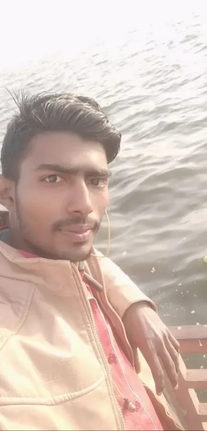 A person in a beige jacket and pink shirt taking a selfie by the lake.