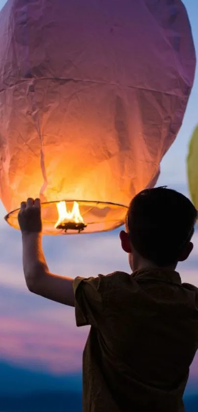 Silhouette of a child releasing a glowing lantern against a twilight sky.