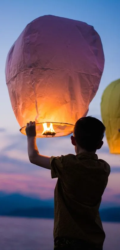 Silhouette of child releasing glowing lantern at dusk over water.