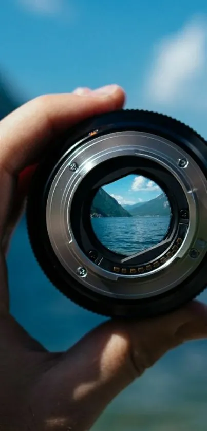 Hand holding a lens with scenic nature view, blue sky, and mountains.