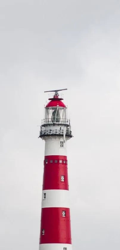 Red and white lighthouse with cloudy sky and coastal dunes.