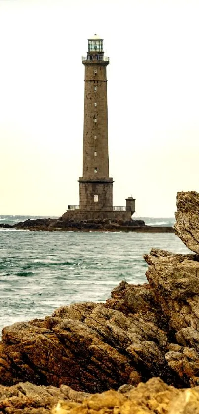 Lighthouse standing tall on a rocky coast with waves and cloudy sky.