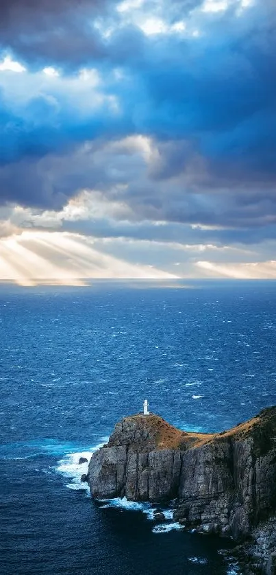 Lighthouse on cliffs with ocean and dramatic sky, sunbeams breaking through clouds.