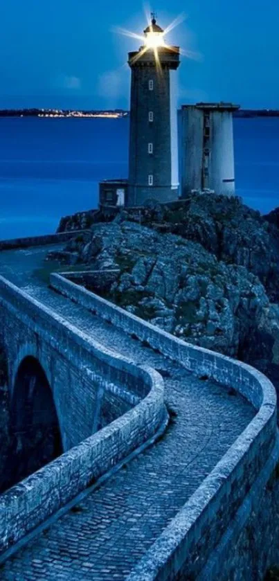 Lighthouse illuminated at dusk on a rocky shore with a winding stone path.