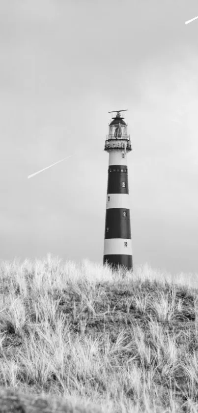 Lighthouse on a grassy hill under a cloudy sky, in black and white.