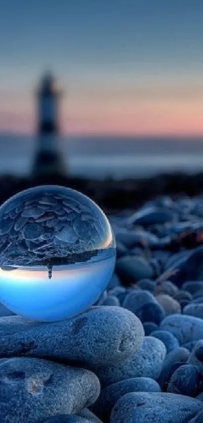 Glass orb with lighthouse reflection on pebble beach.