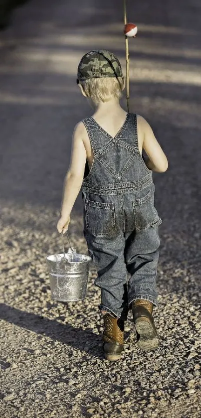 Young boy with bucket and fishing pole on gravel path.