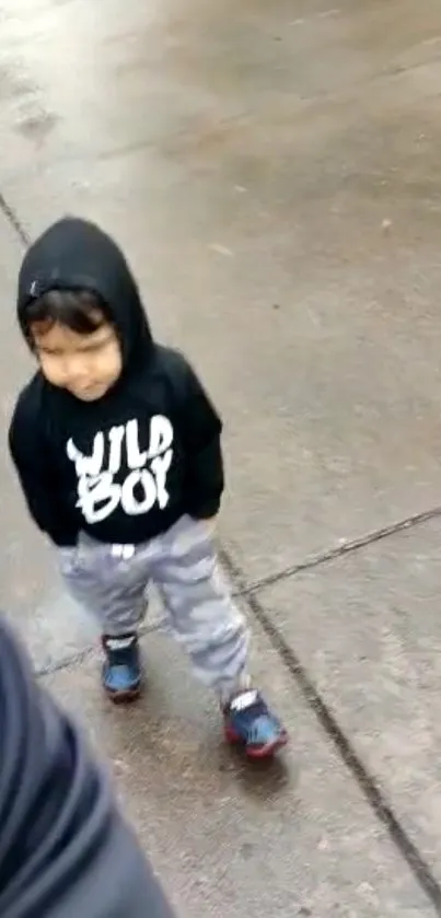 Young child in black hoodie walking on wet path.