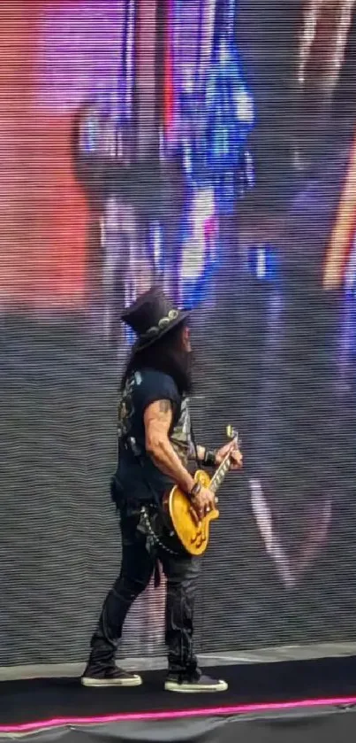 Guitarist performing on stage against a large screen.