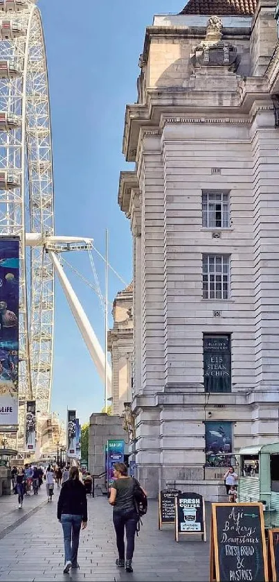 Street view of the London Eye with people walking and historic buildings under clear blue sky.