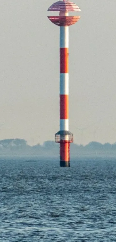 Lone red and white lighthouse in calm ocean.
