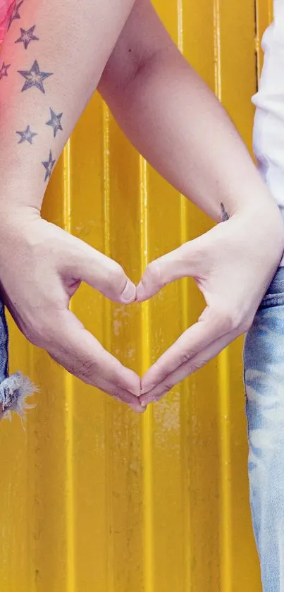 Couple making heart shape with hands on yellow background.