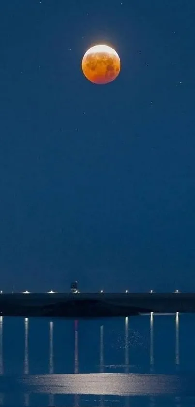 Lunar eclipse over calm waters at night with dark blue sky.