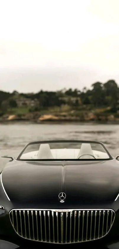 Luxury black car by a calm lakeside with trees in the background.