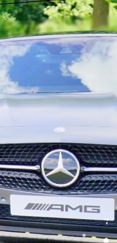 Luxury car front view with Mercedes badge and nature reflection.